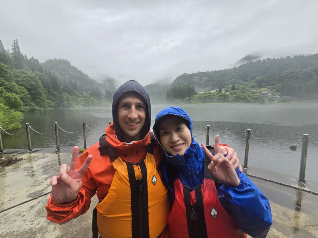雨の中、只見川を背景に笑顔でピースサインのご夫妻