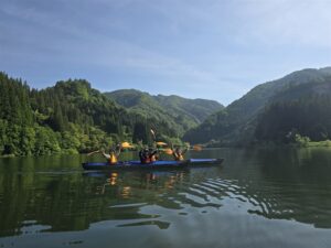 只見川の山並みを背景に、両艇でパドルを掲げて喜ぶ参加者4名