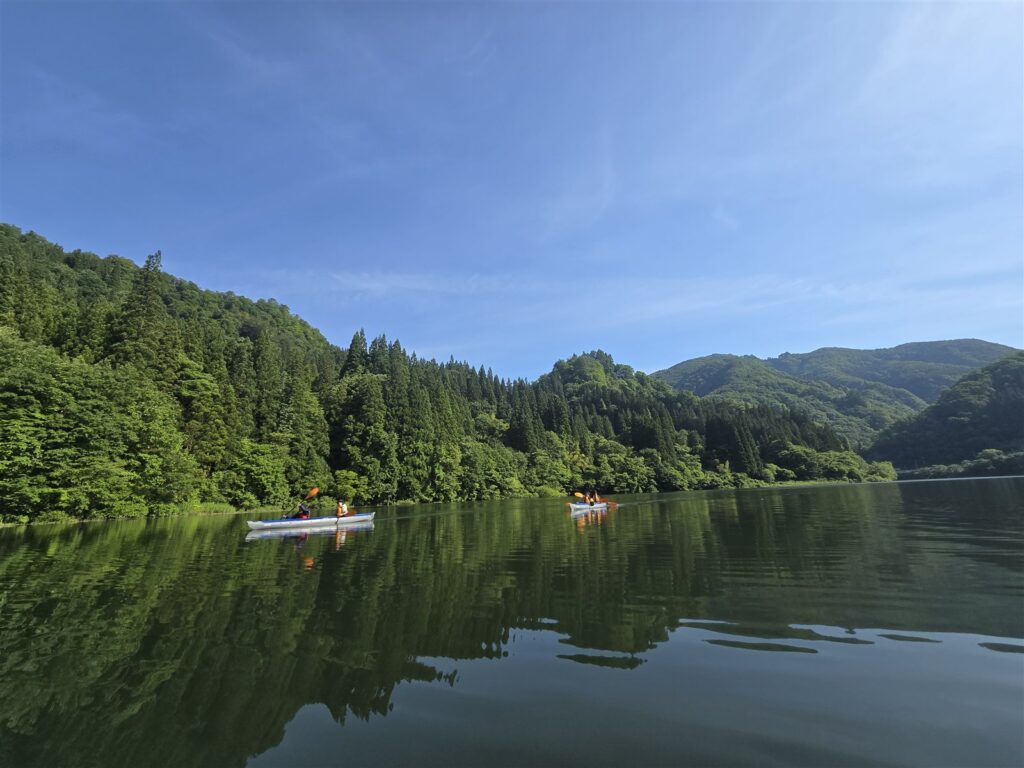 山並みが水面に映り込む只見川と、遠くに小さく見える2艇のカヤック
