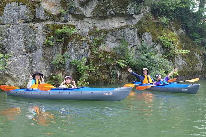 緑の只見川で、岩壁を背に手を振る家族・仲間のグループ