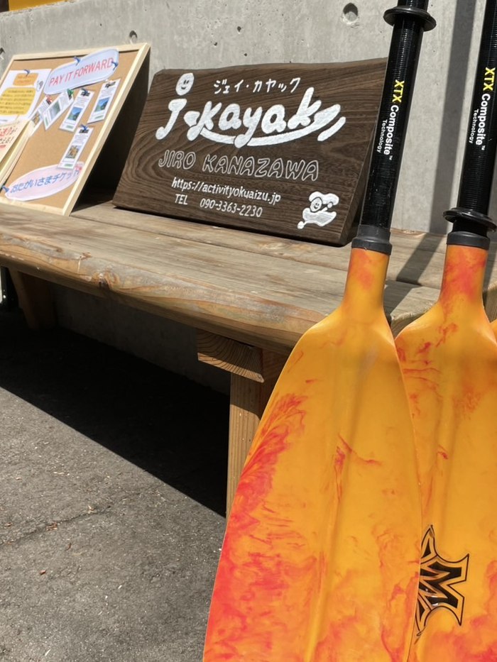 J.Kayakの木製看板と、立てかけられたオレンジのパドル