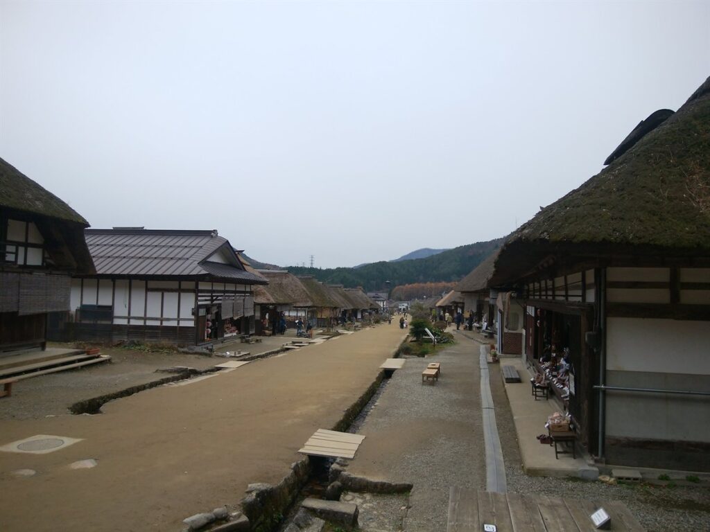 下郷町・大内宿の茅葺き屋根の家並みが続く通り。晩秋で山の木々は落葉しかけている